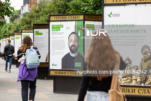 People walk on an alee by posters dedicated to fallen soldiers in Bucha, Ukraine on May 17, 2023. The poster are singed 'Glory to the heroes...