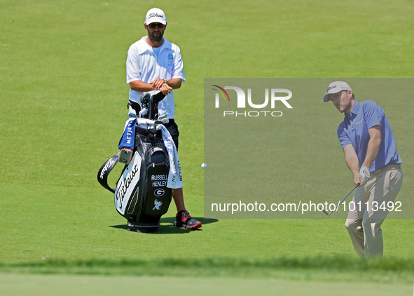 Russell Henley of Columbus, Georgia chips onto the 18th green as his caddie looks on during the first round of the The Memorial Tournament p...