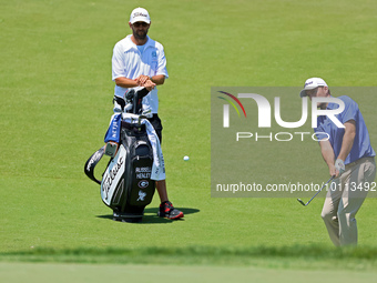 Russell Henley of Columbus, Georgia chips onto the 18th green as his caddie looks on during the first round of the The Memorial Tournament p...