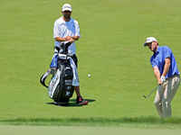 Russell Henley of Columbus, Georgia chips onto the 18th green as his caddie looks on during the first round of the The Memorial Tournament p...