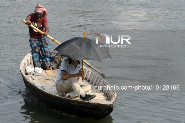 Passengers cross the river Buriganga as they hold an umbrella to prevent suns heat during a heat wave in Dhaka, Bangladesh, May 06, 2023....