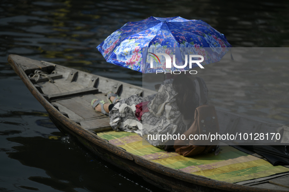 Passengers cross the river Buriganga as they hold an umbrella to prevent suns heat during a heat wave in Dhaka, Bangladesh, May 06, 2023....