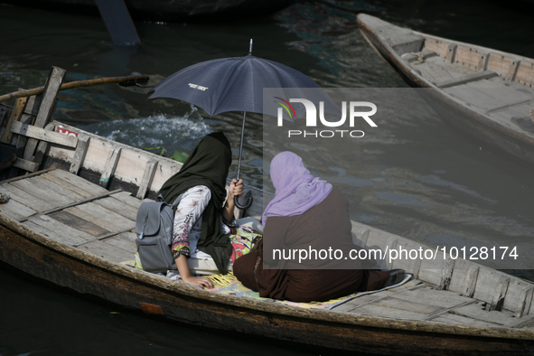 Passengers cross the river Buriganga as they hold an umbrella to prevent suns heat during a heat wave in Dhaka, Bangladesh, May 06, 2023....