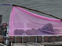 A boatman sleeps under a mosquito net on his boat to protect himself from dengue at the bank of the Buriganga River in Dhaka, Bangladesh, on...