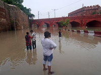 People click pictures near a flooded bridge behind the iconic Red Fort, after a rise in the waters of the river Yamuna due to heavy monsoon...