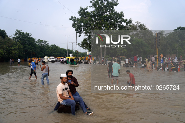 People swim and click pictures as they throng around a flooded road intersection, after a rise in the waters of the river Yamuna due to heav...