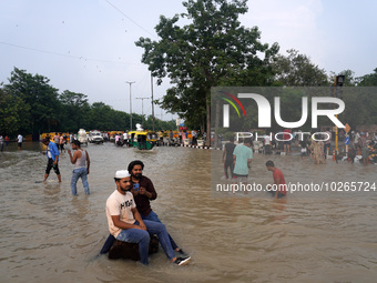 People swim and click pictures as they throng around a flooded road intersection, after a rise in the waters of the river Yamuna due to heav...