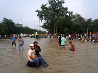 People swim and click pictures as they throng around a flooded road intersection, after a rise in the waters of the river Yamuna due to heav...