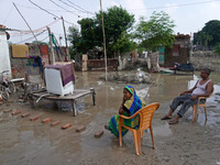 A couple sits outside their flooded house inside a waterlogged street in a low-lying area, after a rise in the waters of river Yamuna due to...