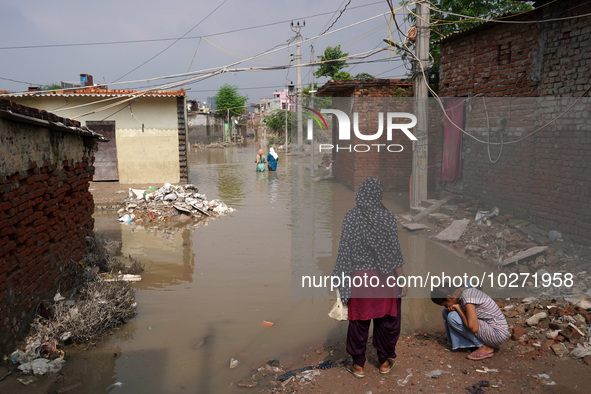 Residents wade through a waterlogged street to reach their homes in a low-lying area, after a rise in the waters of river Yamuna due to heav...