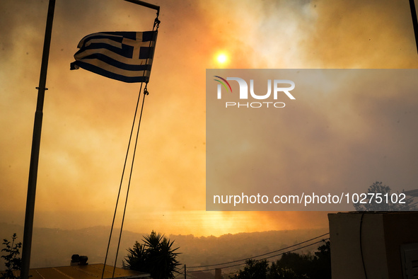 A Greek flag in front of smoke during a wildfire in southern urban of Attica, Greece, on 17, July 2023. Fire fighting forces battling a blaz...