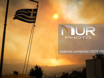 A Greek flag in front of smoke during a wildfire in southern urban of Attica, Greece, on 17, July 2023. Fire fighting forces battling a blaz...