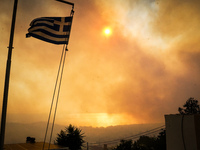 A Greek flag in front of smoke during a wildfire in southern urban of Attica, Greece, on 17, July 2023. Fire fighting forces battling a blaz...