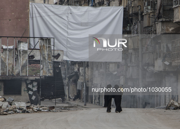 Two women, one carrying a child and they walking near one of curtains  on Bustan Alqasr district in Aleppo city on 1st February 2016.
