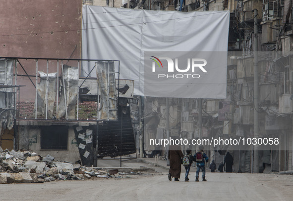 a woman and two children carrying school bags are walking near one of curtains  on Bustan Alqasr district in Aleppo city on 1st February 201...