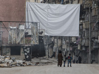 a woman and two children carrying school bags are walking near one of curtains  on Bustan Alqasr district in Aleppo city on 1st February 201...