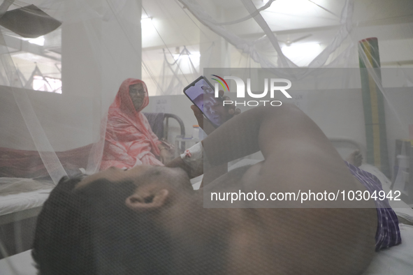 A dengue-infected patient stays under mosquito nets as he makes a video call during his treatment in the Shaheed Suhrawardy Medical College...