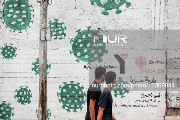  Palestinians walk past street art showing a Covid-19 coronavirus in Gaza City, on August 14, 2023. The number of new Covid-19 cases reporte...