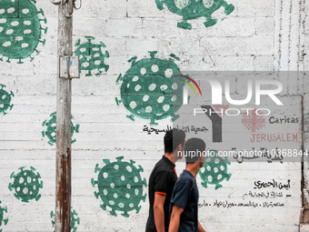  Palestinians walk past street art showing a Covid-19 coronavirus in Gaza City, on August 14, 2023. The number of new Covid-19 cases reporte...