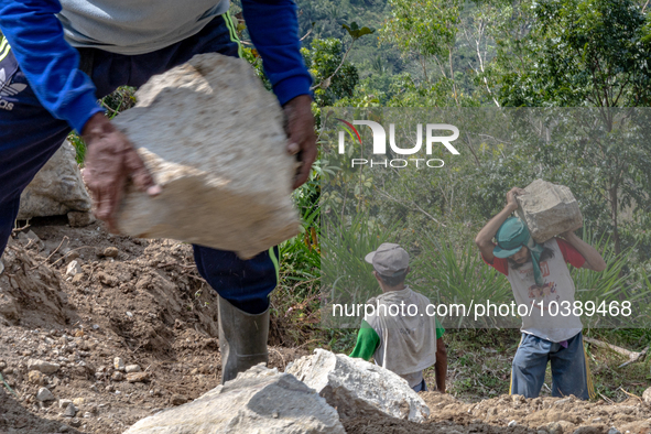 A man carries a big stone as he helps villagers to renovate a broken village road at Kebumen, Central Java, Indonesia on August 20, 2023.  