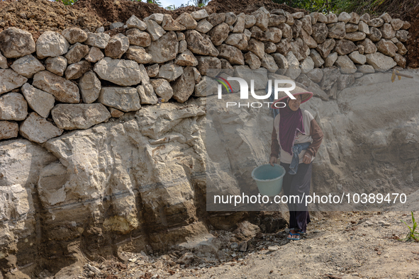 A woman stands in a broken road during the road renovation at Kebumen, Central Java, Indonesia on August 20, 2023.  