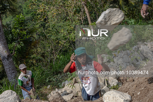 A man throws a big stone as he helps villagers to renovate a broken village road at Kebumen, Central Java, Indonesia on August 20, 2023.  