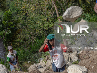 A man throws a big stone as he helps villagers to renovate a broken village road at Kebumen, Central Java, Indonesia on August 20, 2023.  (