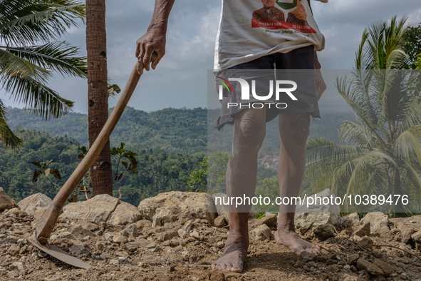 A man holds a hoe, as he helps villagers to renovate a broken village road at Kebumen, Central Java, Indonesia on August 20, 2023.  