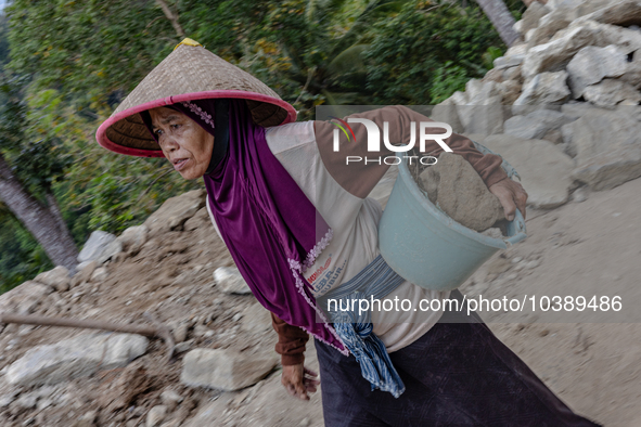 A woman carries a bucket of sand and stone as she helps villagers to renovate a broken village road at Kebumen, Central Java, Indonesia on A...