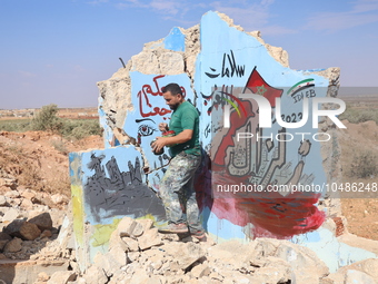 Graffiti artist Aziz Al-Asmar paints a painting on the wall of a destroyed house in the town of bench rural Idlib in solidarity with the vic...