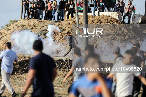 A Palestinian protester throws back a tear gas fired by Israeli security forces along the border fence during clashes with Israeli forces in...