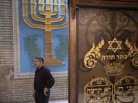 An Iranian-Jewish man stands next to a Menorah and a Star of David (The Jewish symbols) during a gathering at a synagogue in downtown Tehran...