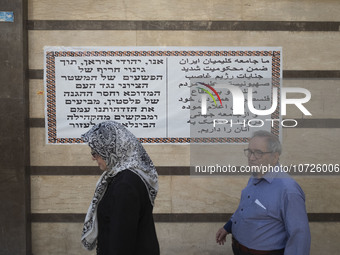 An Iranian-Jewish man and a Jewish woman walk past a banner hanged on a wall of a synagogue in downtown Tehran during a gathering to protest...