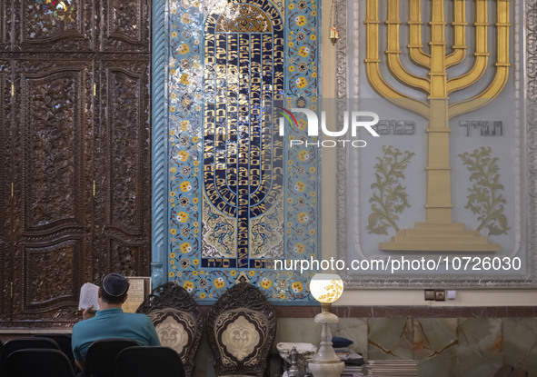 An Iranian-Jewish man reads a Hebrew Bible while sitting next to a Menorah (A Jewish symbol) at a synagogue in downtown Tehran before a gath...