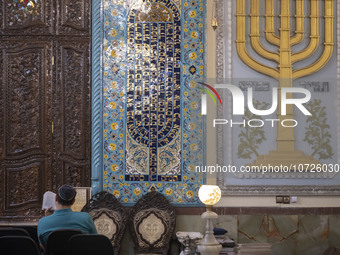 An Iranian-Jewish man reads a Hebrew Bible while sitting next to a Menorah (A Jewish symbol) at a synagogue in downtown Tehran before a gath...