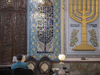 An Iranian-Jewish man reads a Hebrew Bible while sitting next to a Menorah (A Jewish symbol) at a synagogue in downtown Tehran before a gath...