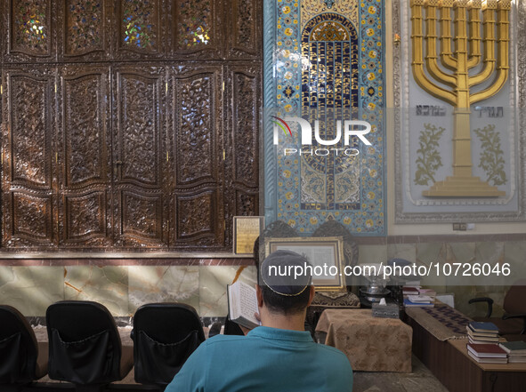 An Iranian-Jewish man reads a Hebrew Bible while sitting next to a Menorah (A Jewish symbol) at a synagogue in downtown Tehran before a gath...