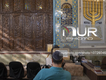 An Iranian-Jewish man reads a Hebrew Bible while sitting next to a Menorah (A Jewish symbol) at a synagogue in downtown Tehran before a gath...