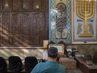 An Iranian-Jewish man reads a Hebrew Bible while sitting next to a Menorah (A Jewish symbol) at a synagogue in downtown Tehran before a gath...