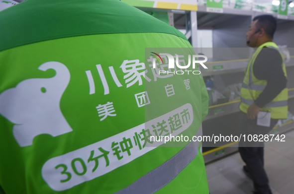 A Meituan employee is walking out of the front warehouse of Xiaoxiang Supermarket to deliver goods to customers in Hangzhou, Zhejiang Provin...