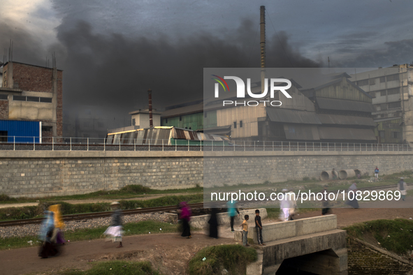 People are walking past an iron industry that is emitting toxic smoke into the air in the early morning in Dhaka, Bangladesh, on December 4,...