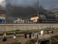 People are walking past an iron industry that is emitting toxic smoke into the air in the early morning in Dhaka, Bangladesh, on December 4,...