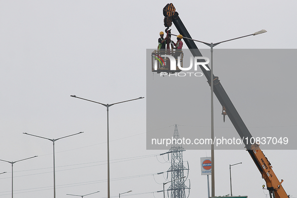 An electrician is working on upgrading an LED street lamp to integrate it with a smart system under a cloudy sky on National Highway 6 in We...