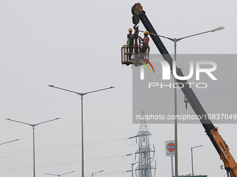 An electrician is working on upgrading an LED street lamp to integrate it with a smart system under a cloudy sky on National Highway 6 in We...