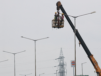 An electrician is working on upgrading an LED street lamp to integrate it with a smart system under a cloudy sky on National Highway 6 in We...