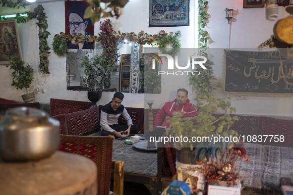 An Iranian man is puffing on a water pipe while sitting next to his friend at a traditional restaurant in the flooded village of Imamzadeh D...