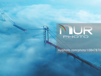 Workers are hoisting a steel girder of the main bridge in the clouds at the Zangke River Bridge on the expressway in Bijie, Guizhou Province...