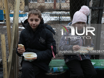 In Kyiv, Ukraine, on December 18, 2023, a boy and a girl are having dinner in the yard outside the residential building at 4A Ostafiia Dashk...