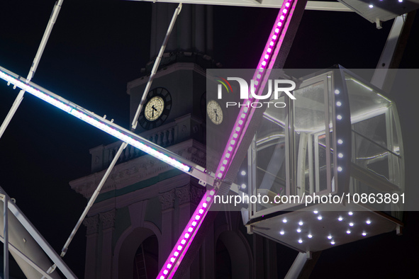 A cabin of the Ferris wheel is seen near a clock tower at night in Kontraktova Square, Kyiv, Ukraine, on December 18, 2023. 