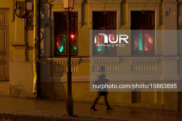 A woman is walking past an old building while red and green lights are illuminating three windows at night in Kyiv, Ukraine, on December 18,...